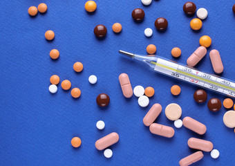 Thermometer and pills on a blue background.