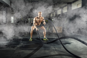 Athletic young man with battle rope doing exercise in the fitness gym. Sports concept.