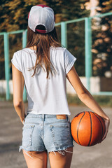 Pretty young girl holding basketball ball, rear view.