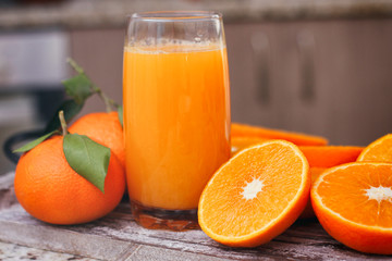 Glass with fresh citrus juice. Halves of tangerines and full fruits with leaves. Wood food stand.