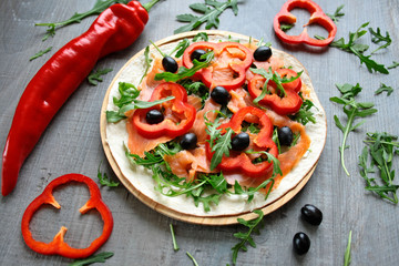 Tortilla posmarowana sosem chrzanowym, przykryta wędzonym łososiem, rukolą, papryką, i czarnymi oliwkami