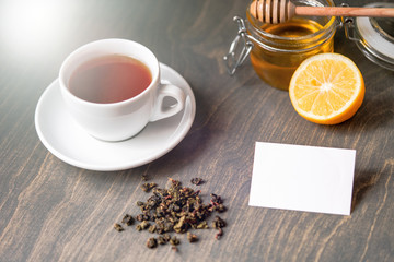 Tea with lemon and honey on wooden rustic table with blank business card.