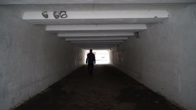 Man walking through the dark pedestrian underground crossing tunnel with light at the end and number of the beast 666 on the wall