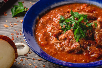 Veal meat with spices in a tomato sauce, veal meat in tomato sauce with onion, garlic, chili peper on the wooden background. boiled meat and fresh tomato top view