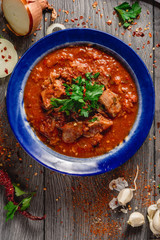 Stewed veal meat with spices in a tomato sauce, veal meat in tomato sauce with onion, garlic, chili peper on the wooden background. boiled meat and fresh tomato top view