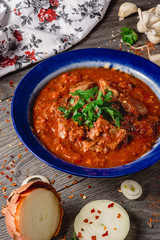Stewed veal meat with spices in a tomato sauce, veal meat in tomato sauce with onion, garlic, chili peper on the wooden background. boiled meat and fresh tomato horizontal view