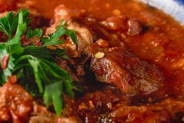 Stewed veal meat with spices in a tomato sauce, veal meat in tomato sauce with onion, garlic, chili peper on the wooden background. boiled meat and fresh tomato horizontal view