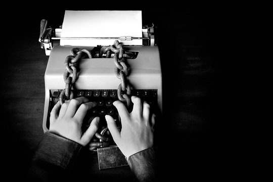 Information censorship - Hands writing on a typewriter locked with a chain