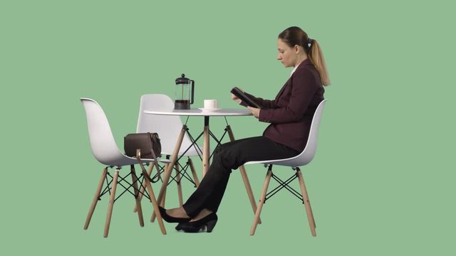 Young alone woman sitting at a table and reading an e-book. Video with alpha channel