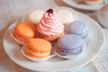 a plate gives colorful macarons on the table orange, blue, white