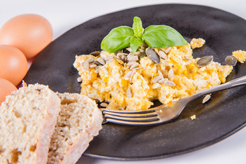 Scrambled eggs with sunflower and pumpkin seeds, some fresh eggs and wholemeal bread, eaten with a fork, decorated with basil, on a white background