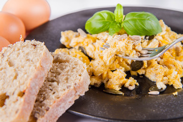 Scrambled eggs with sunflower and pumpkin seeds, some fresh eggs and wholemeal bread, eaten with a fork, decorated with basil, on a white background