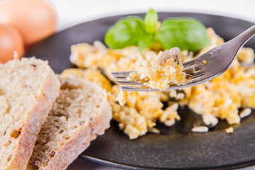 Scrambled eggs with sunflower and pumpkin seeds, some fresh eggs and wholemeal bread, eaten with a fork, decorated with basil, on a white background