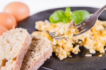 Scrambled eggs with sunflower and pumpkin seeds, some fresh eggs and wholemeal bread, eaten with a fork, decorated with basil, on a white background