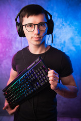 Computer nerd with keyboard over colorful pink and blue neon lit wall