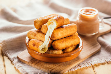 Cheese fingers, typical Venezuelan appetizer called tequeños accompanied with a pink sauce on a wooden board