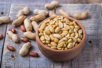 Peanuts in small wooden bowl on natural rustic desk.