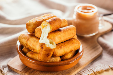 Cheese fingers, typical Venezuelan appetizer called tequeños accompanied with a pink sauce on a wooden board