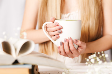 Fototapeta na wymiar A Cup of tea in women's hands. Concept for spring morning. Flower tea in a white Cup on the table with books and flowers