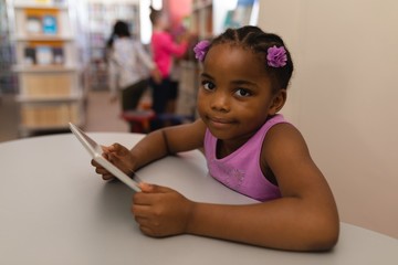 Schoolgirl with digital tablet looking at camera on table in