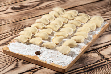 Raw dumplings on wooden cutting board, is ready to boil. Also known as Vareniks. Ukrainian traditional cuisine