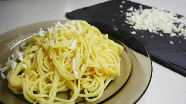 Woman hand sprinkle spaghetti with grated mozzarella cheese in slow motion.