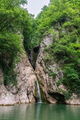 A high waterfall falls from a cliff into a clear lake