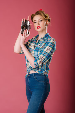 Portrait of a girl dressed in vintage clothing holding old fashioned camera on the pink background. Pinup portrait