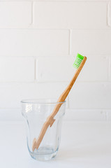 Single bamboo toothbrush in glass on white table with copy space