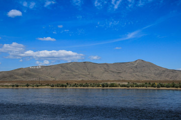 The great Russian river Yenisei which originates in the Siberian region in the center of Asia - Tyva. Bright summer sunny day, clear sky with clouds and bright blue water of the river.