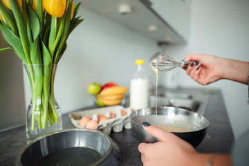 Girl cooking pancakes in the kitchen, home with flowers, eggs, fruits on the table.