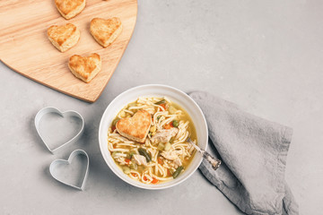 Heart-Shaped Homemade Biscuits with Homemade Chicken-Noodle Soup on Gray Background