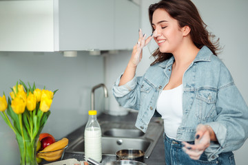 Girl cooking pancakes in the kitchen, home with flowers, eggs, fruits on the table.