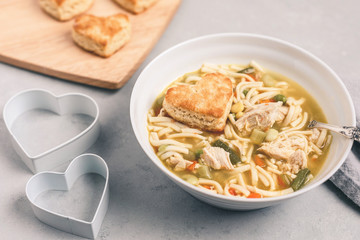 Heart-Shaped Homemade Biscuits with Homemade Chicken-Noodle Soup on Gray Background