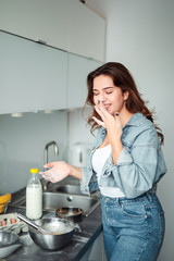 Girl cooking pancakes in the kitchen, home with flowers, eggs, fruits on the table.