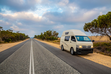 Fototapeta na wymiar Campervan in Australia standing at the site of straight, endless road in late afternoon