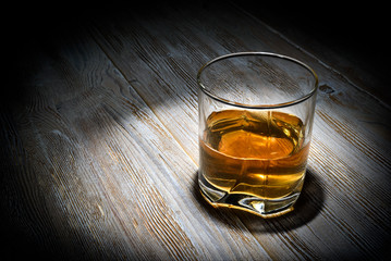 Glass of whiskey on a vintage wooden table on a black background.