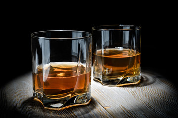 Two glasses of whiskey on a vintage wooden table on a black background.