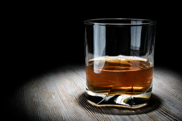 Glass of whiskey on a vintage wooden table on a black background.