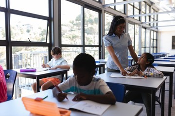 Female teacher teaching schoolkid at desk in classroom