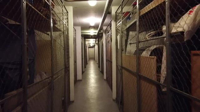 Walking in a narrow cellar corridore with pipes in the ceiling and storages on each side. Filmed in realtime at 4k.