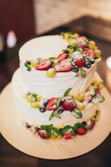 Three parts naked wedding cake with fruits and berries.