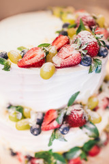 Three parts naked wedding cake with fruits and berries.