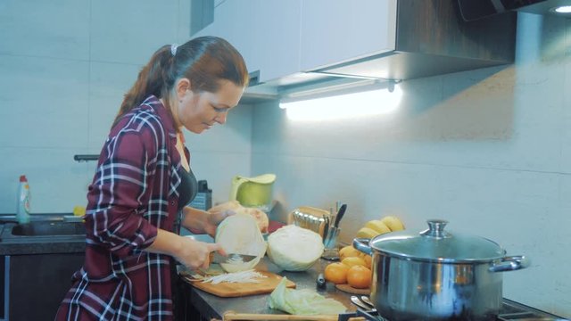 woman in the kitchen preparing a meal concept. girl in the kitchen cuts cabbage with a knife. cook vegetarian food healthy food. girl lifestyle at home in the kitchen slow motion video