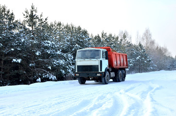 Cargo dump truck rides on a snowy road to load sand into career. Winter road against the backdrop of fabulous spruce trees in the snow and blue sky