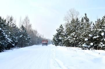 Cargo dump truck rides on a snowy road to load sand into career. Winter road against the backdrop of fabulous spruce trees in the snow and blue sky