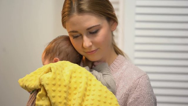Young mother holding adorable baby in arms, artificial feeding, newborn care