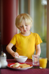 Little boy eating healthy breakfast in hotel restaurant.