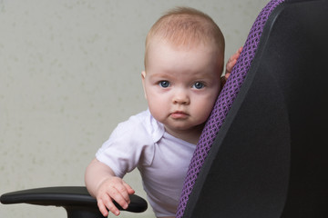 baby is standing on the office chair and holding the armrest