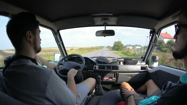 Professional wide angle shot of two men driving a car through countryside in the morning. Two handsome guys taking a road trip in the countryside. Fish-eye view.